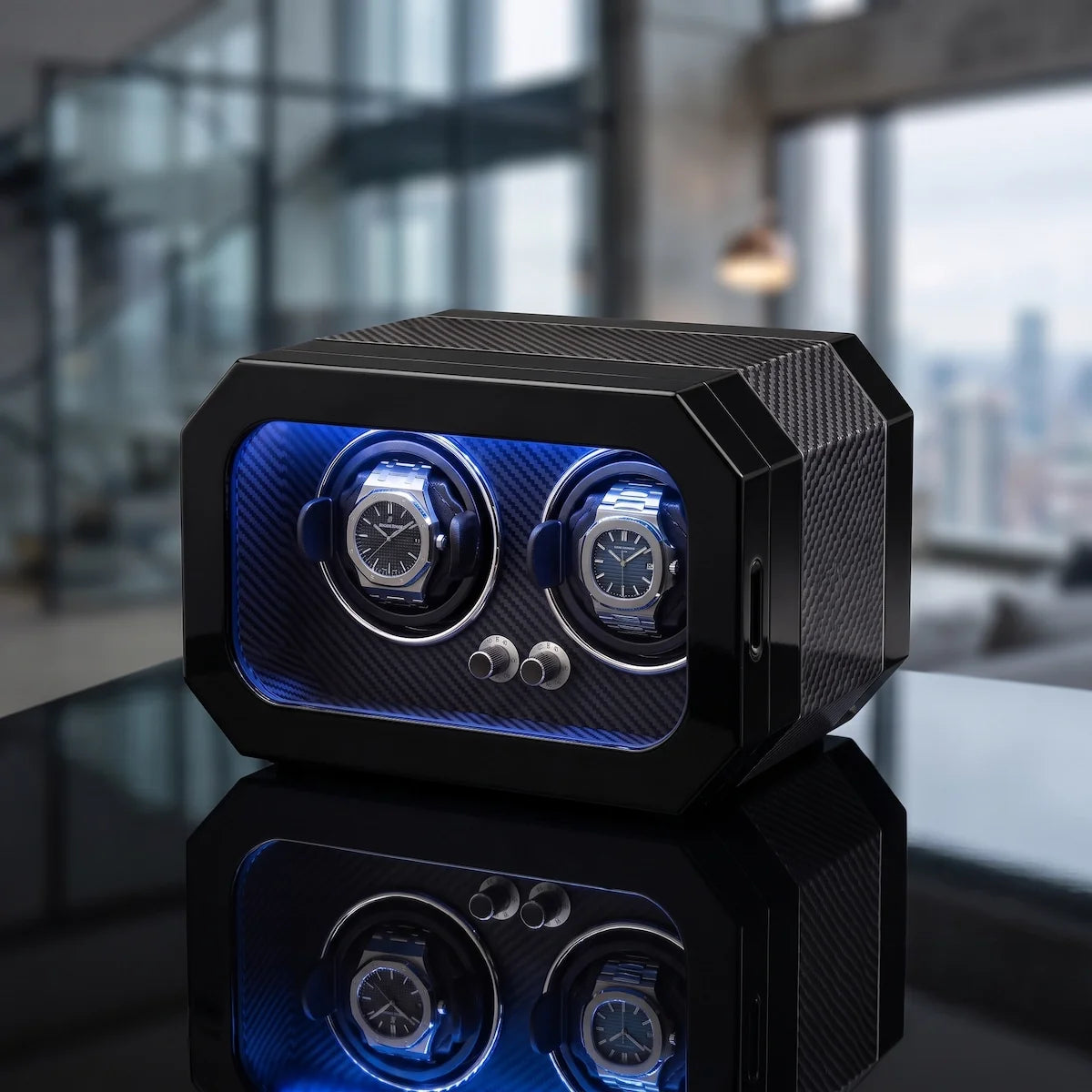 Remontoir noir en fibre de carbone pour 2 montres avec éclairage LED bleu et moteur silencieux sur une surface réfléchissante.