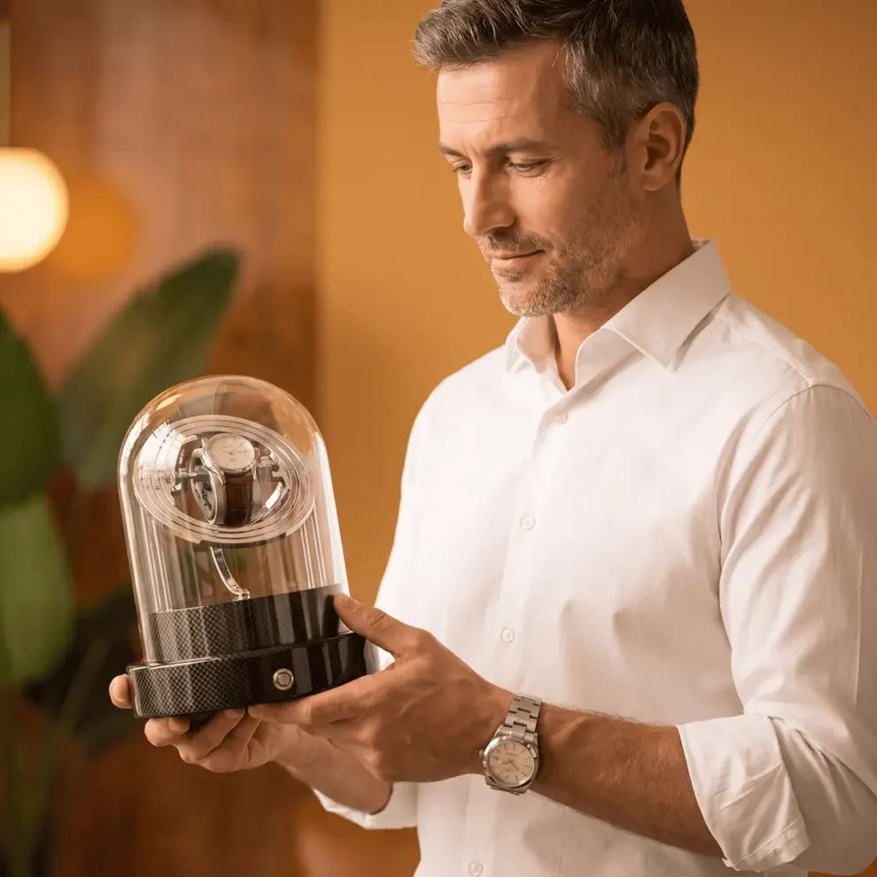 Remontoir Astronome Comète noir en fibre de carbone avec dôme en verre, tenant une montre automatique dans un intérieur élégant.