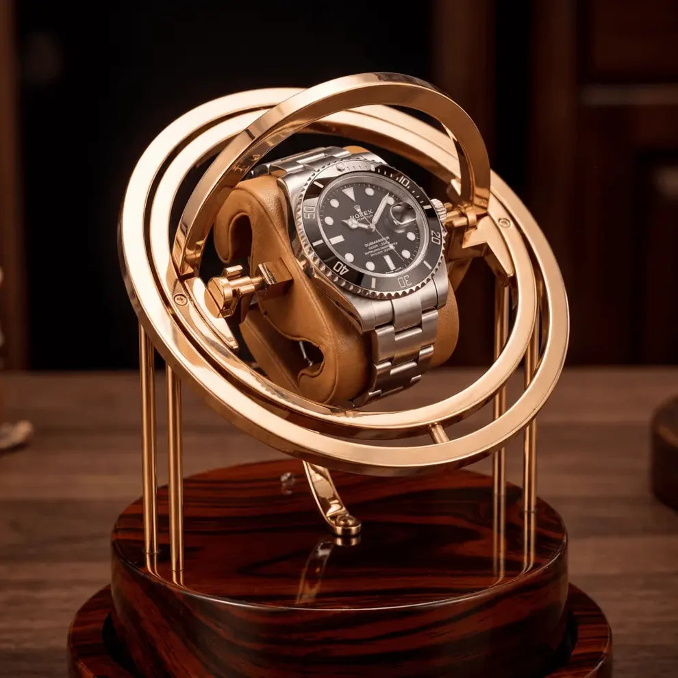Remontoir Astronome Prestige doré avec structure rotative en métal et socle en bois sombre pour une montre automatique.