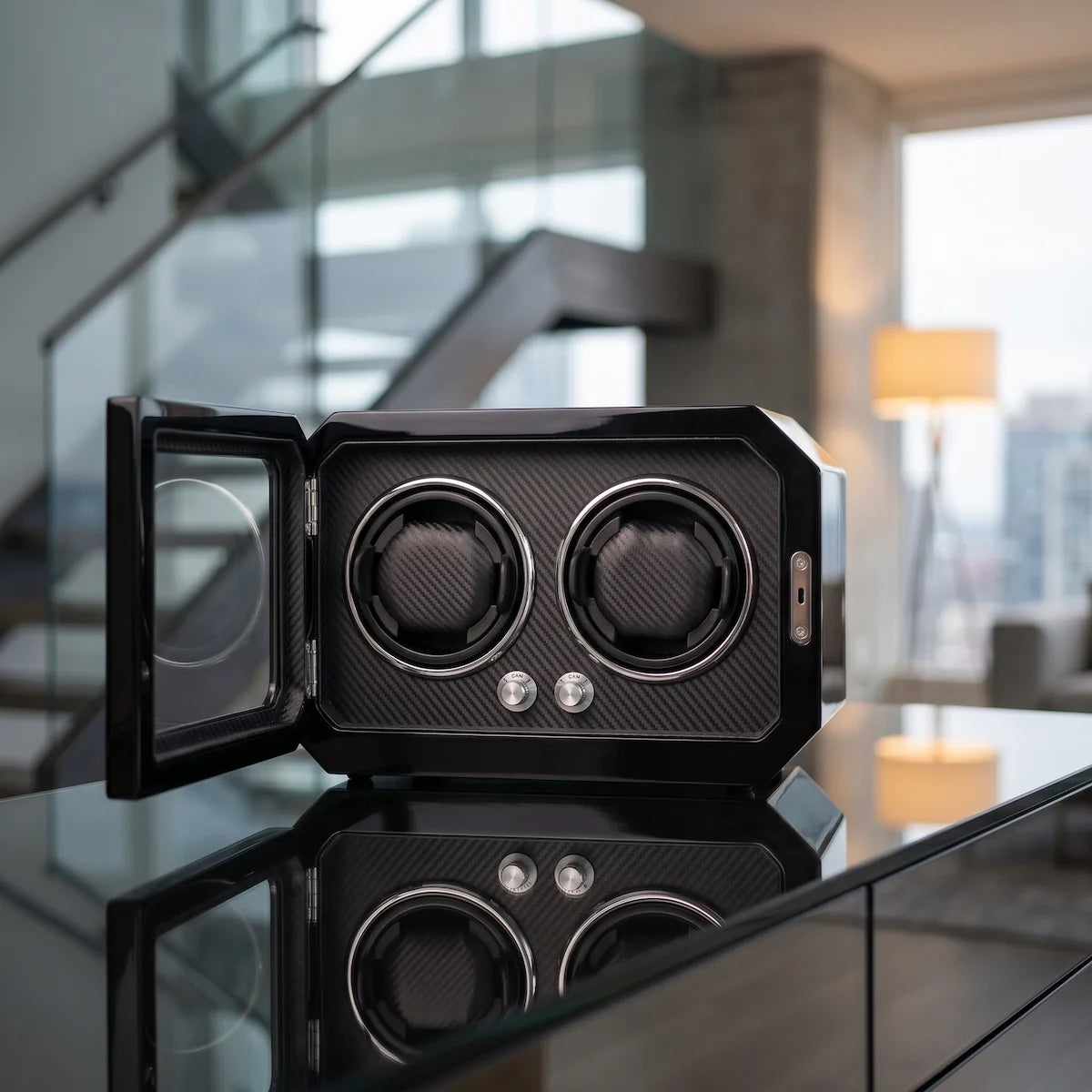 Remontoir pour 2 montres en fibre de carbone noire avec porte vitrée et éclairage LED, posé sur une table moderne.