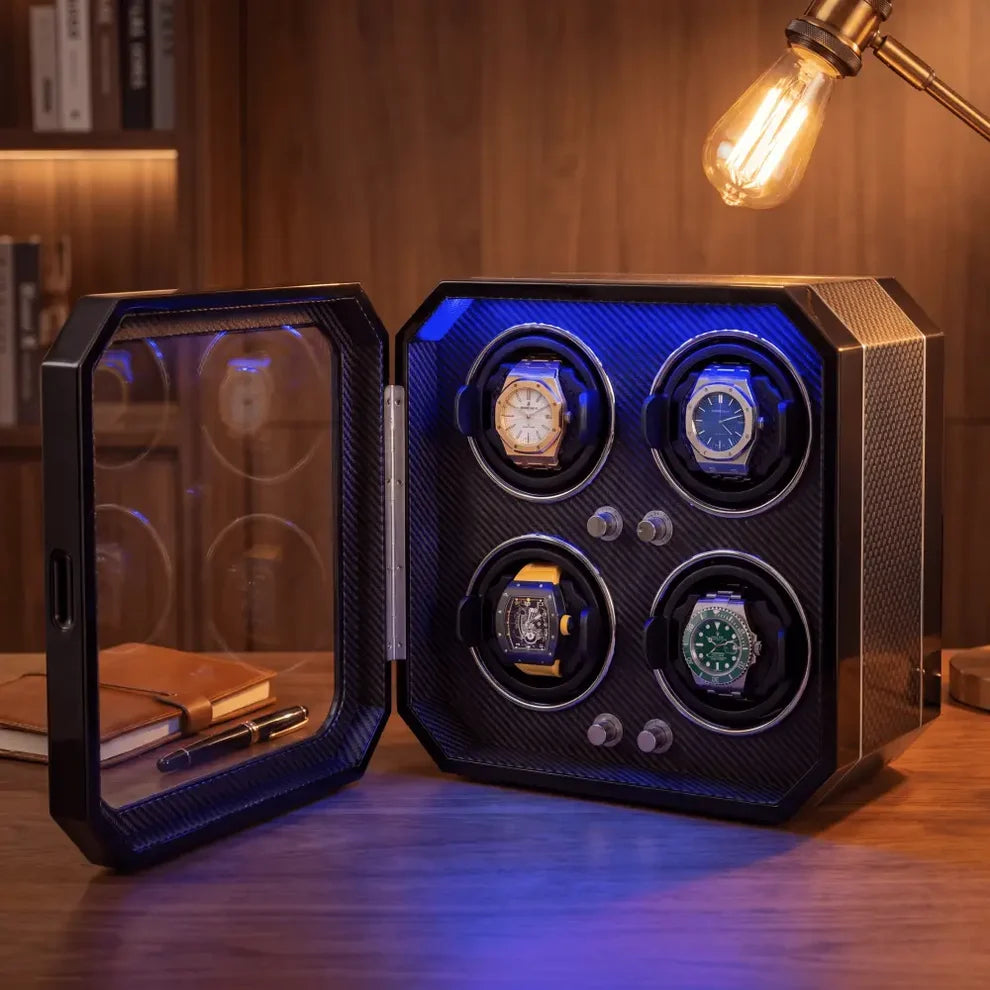 Remontoir pour 4 montres en fibre de carbone noire avec éclairage LED bleu et porte vitrée, posé sur un bureau en bois.