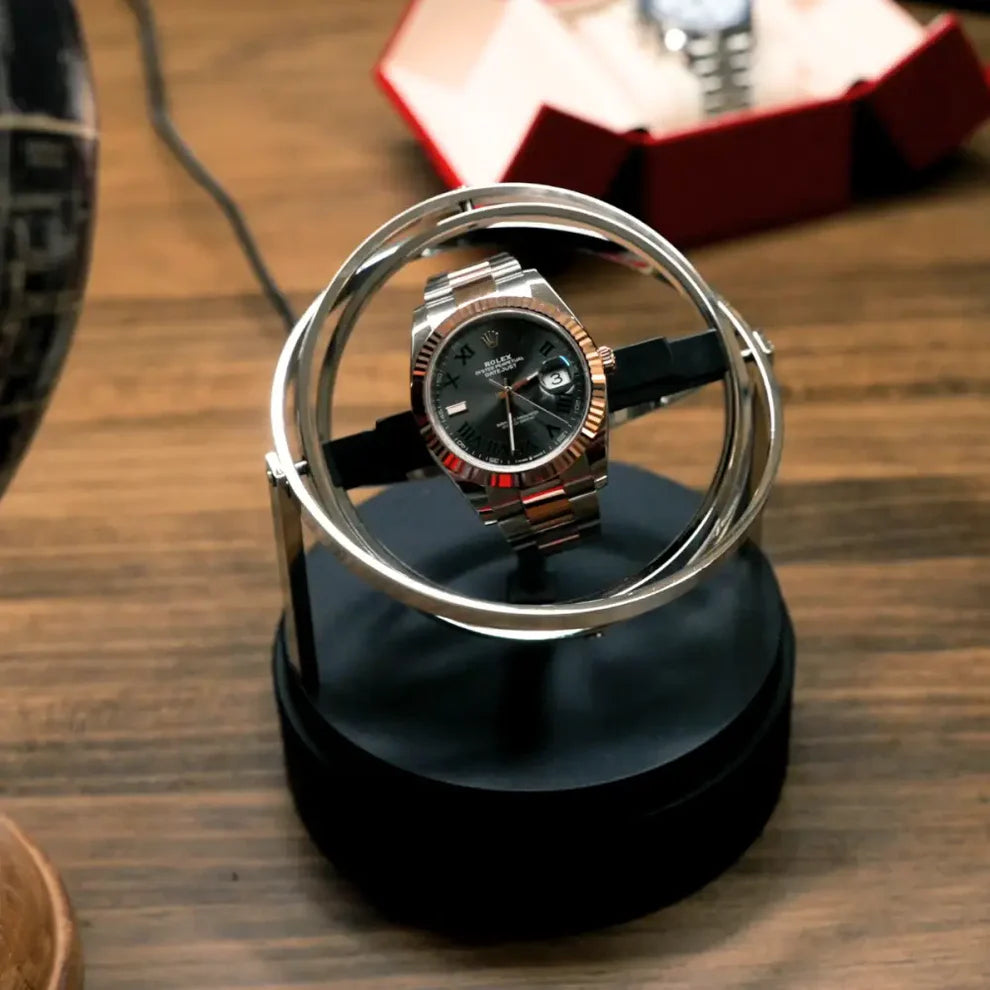Remontoir automatique Astronome doré en acier avec design circulaire moderne pour une montre sur socle noir.