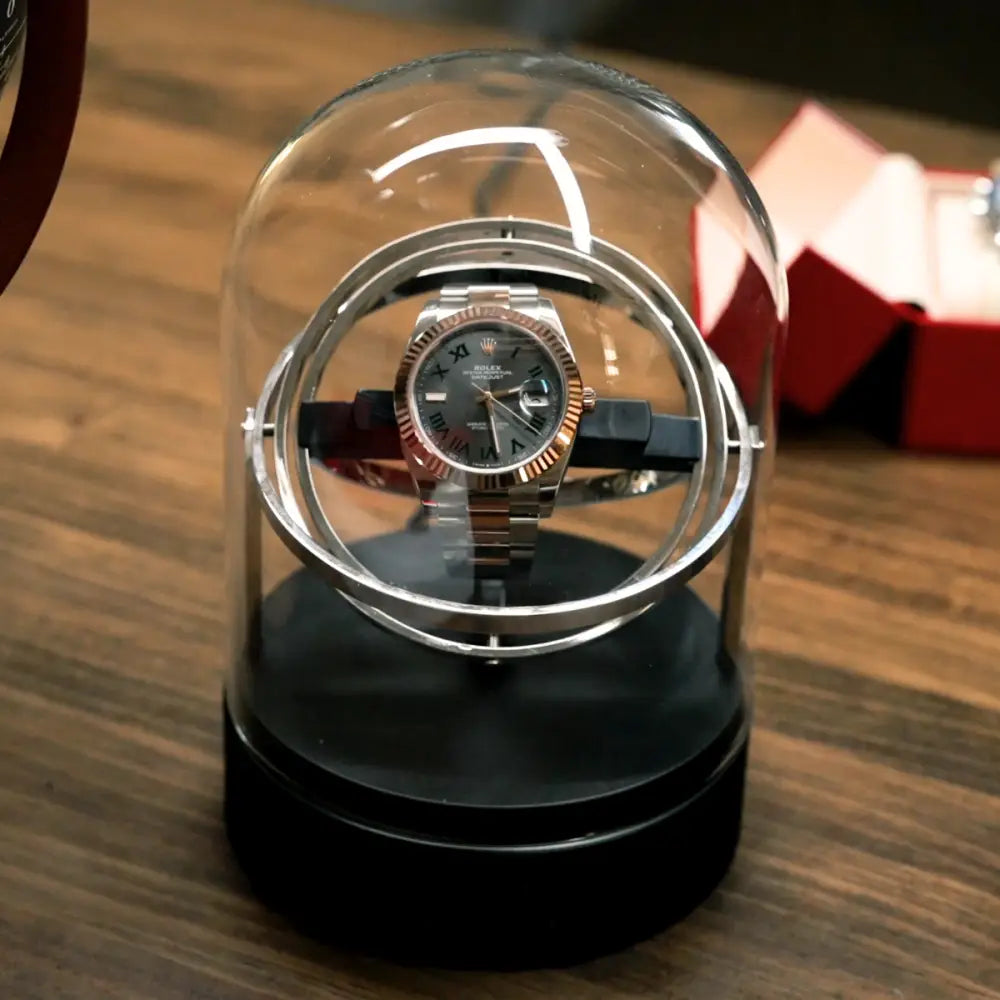Remontoir automatique Astronome en acier argenté sous cloche en verre, design rotatif moderne pour montre de luxe.