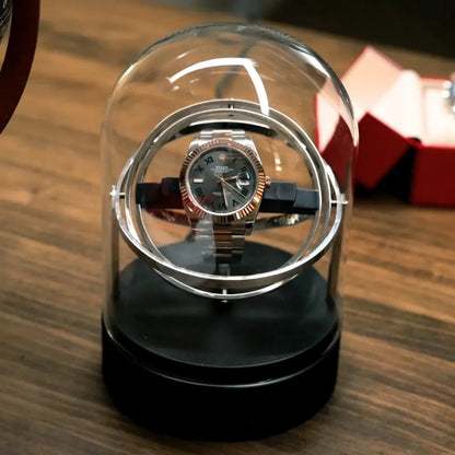 Remontoir automatique Astronome en acier argenté sous cloche en verre, design rotatif moderne pour montre de luxe.