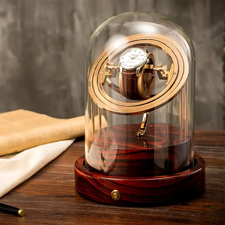 Remontoir automatique Astronome Prestige doré et bois rouge sous cloche en verre pour une montre.